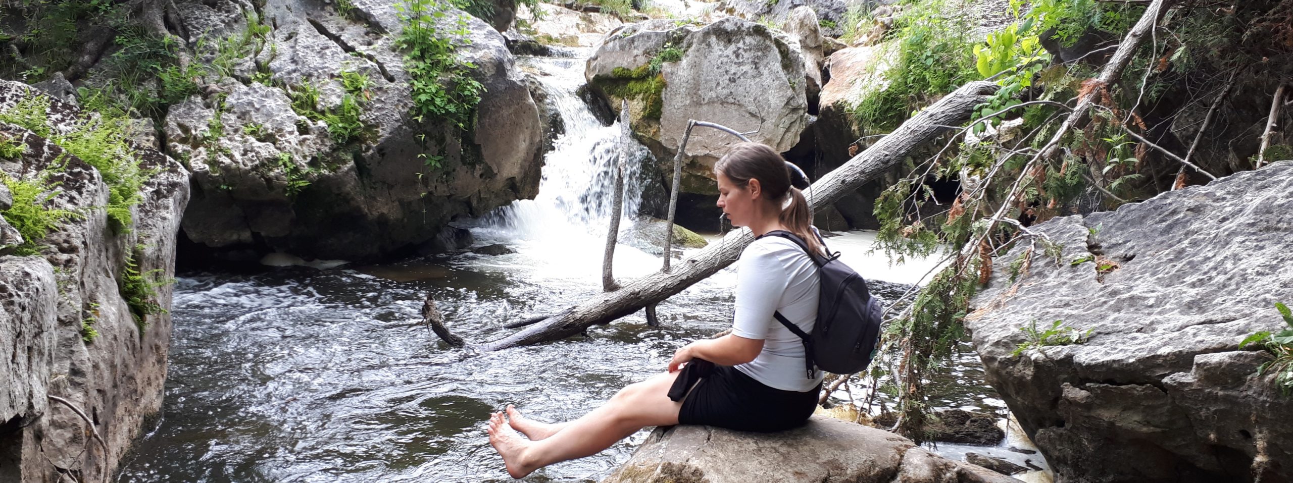woman barefoot sitting beside waterfall